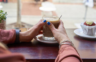 Frau hält Kaffeetasse auf Tisch in Cafeteria - VEGF04211