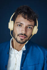 Young man wearing headphones against blue background - JOSEF04016