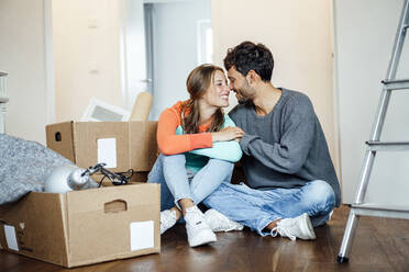 Smiling young couple sitting together by cardboard box at home - JOSEF04026