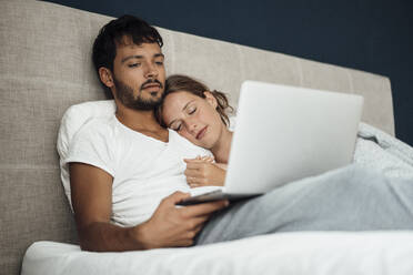 Junger Mann benutzt Laptop bei seiner Freundin, die zu Hause auf dem Bett schläft - JOSEF04027