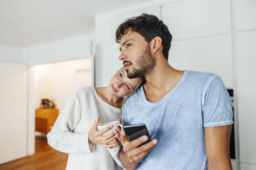 Young man with smart phone standing by girlfriend while looking away - JOSEF04046