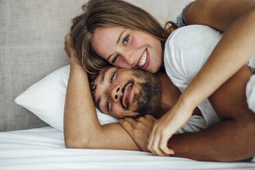 Beautiful smiling woman lying down with boyfriend on bed - JOSEF04057