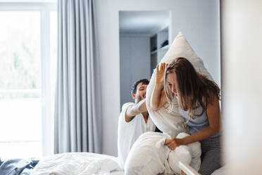 Happy playful couple having pillow fight in bedroom - JOSEF04069