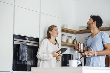 Cheerful young couple looking at each other while standing in domestic kitchen - JOSEF04071