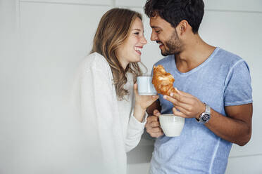 Lächelnder gut aussehender Mann mit Croissant und Kaffeetasse, der seine Freundin anschaut - JOSEF04078