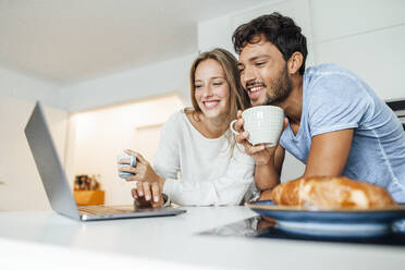 Young couple using laptop in kitchen at home - JOSEF04087