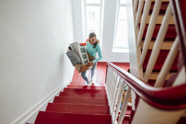 Junge Frau, die Kartons trägt, während sie zu Hause die Treppe hinaufgeht - JOSEF04100
