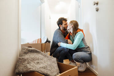 Affectionate couple kissing by box at home - JOSEF04103