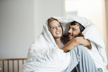 Happy couple sitting under blanket at home - JOSEF04111