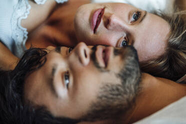 Girlfriend and boyfriend looking up while lying on bed at home - JOSEF04115