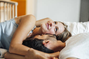 Man kissing girlfriend looking up while lying on bed at home - JOSEF04117