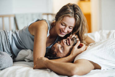 Playful young couple lying on bed at home - JOSEF04118