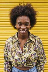 Lächelnde erwachsene Frau vor einem gelben Fensterladen stehend - JRVF00427