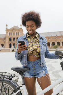 Frau benutzt Mobiltelefon, während sie mit dem Fahrrad auf dem Gehweg steht - JRVF00441