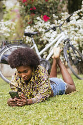 Woman using mobile phone while lying on grass in garden - JRVF00446