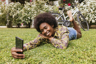 Schöne Frau, die ein Selfie durch ein Smartphone macht, während sie im Park liegt - JRVF00447