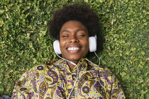 Lächelnde Frau hört Musik über Kopfhörer, während sie im Gras liegt - JRVF00449
