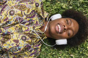 Beautiful woman with headphones smiling while lying on grass - JRVF00450