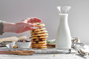 Crop anonyme Hausfrau Stapeln köstliche hausgemachte Kekse mit Schokolade-Chips auf dem Tablett mit Glas frische Milch in der Küche - ADSF22840