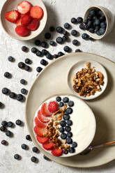 Draufsicht auf eine leckere gesunde Frühstücksschüssel mit weißem Joghurt und frischen Erdbeeren und Blaubeeren mit Granola - ADSF22844