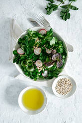 Draufsicht auf einen frischen, gesunden Gemüsesalat in einer Schüssel auf dem Tisch mit Olivenöl und Sonnenblumenkernen - ADSF22846
