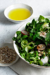 Draufsicht auf einen frischen, gesunden Gemüsesalat in einer Schüssel auf dem Tisch mit Olivenöl und Sonnenblumenkernen - ADSF22847