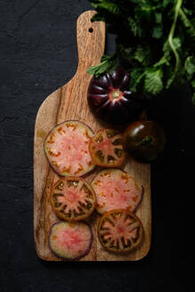 Draufsicht auf frische reife geschnittene schwarze Tomaten und grüne Minzstängel auf hölzernem Schneidebrett auf schwarzem Hintergrund - ADSF22851