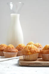 Leckere hausgemachte frisch gebackene süße Muffins in Papierbechern auf dem Tisch mit einem Glas frischer Milch angeordnet - ADSF22854