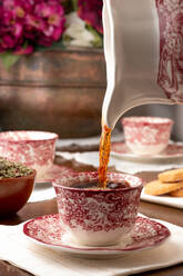Aromatischer heißer Tee, der in eine Keramiktasse gegossen wird, die auf dem Frühstückstisch zu Hause steht - ADSF22860