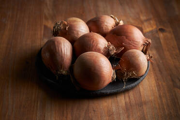 High angle of bunch of fresh unpeeled onions placed on plate on timber table - ADSF22868