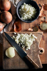 Draufsicht auf eine rustikale Schale mit geschnittenen Zwiebelstückchen, die neben einem Messer auf einem Holztisch in der Küche liegt - ADSF22876
