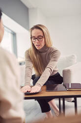 Female psychologist with plate gesticulating and giving advice to unrecognizable client during psychotherapy appointment - ADSF22885