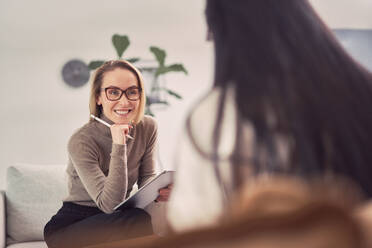 Fröhliche Beraterin, die einem anonymen Klienten zuhört, während sie bei einer psychotherapeutischen Sitzung hilft - ADSF22886