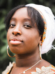 Seitenansicht einer jungen Afrikanerin mit Kopftuch, die im Sommer gegen eine Pflanze in die Kamera schaut - ADSF22903