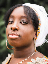 Side view of young African female in kerchief looking at camera against plant in summer - ADSF22903