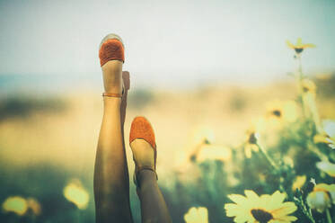 Anonymous female in summer shoes swinging legs against projection of field with yellow flowers - ADSF22948