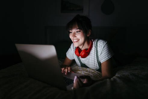 Smiling woman watching movie in darkroom - TCEF01767