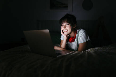 Smiling woman using laptop at darkroom - TCEF01769