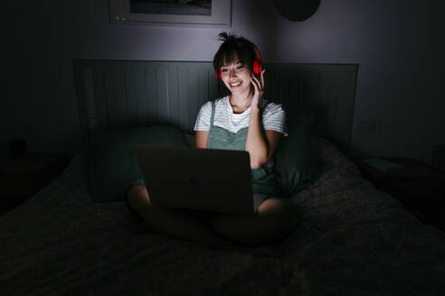 Smiling woman wearing headphones using laptop at home - TCEF01773