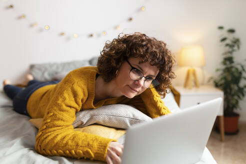 Frau benutzt Laptop, während sie zu Hause auf dem Bett liegt - JPTF00751
