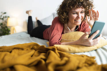 Lächelnde Frau macht Videoanruf über Smartphone im Schlafzimmer - JPTF00764