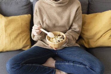 Woman having breakfast while sitting on sofa at home - JPTF00766