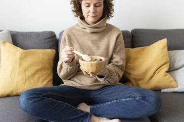 Reife Frau frühstückt zu Hause auf dem Sofa sitzend - JPTF00767