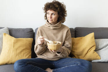 Woman with food bowl looking away in living room - JPTF00768