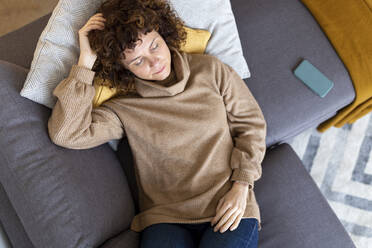 Frau entspannt sich mit ihrem Handy auf dem Sofa im Wohnzimmer zu Hause - JPTF00773