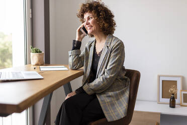 Female freelancer talking on smart phone while sitting on chair at home - JPTF00781