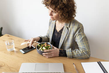 Female freelancer using smart phone while having food at home - JPTF00783