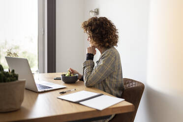 Mature female freelancer having food while sitting at table with laptop - JPTF00784