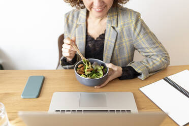 Female freelancer holding bowl of food on table at home - JPTF00786