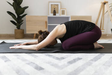 Frau kniend und Yoga auf Übungsmatte zu Hause praktizierend - JPTF00790